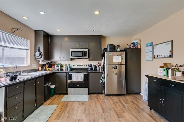kitchen featuring stainless steel appliances, a sink, light wood-type flooring, recessed lighting, and dark cabinets