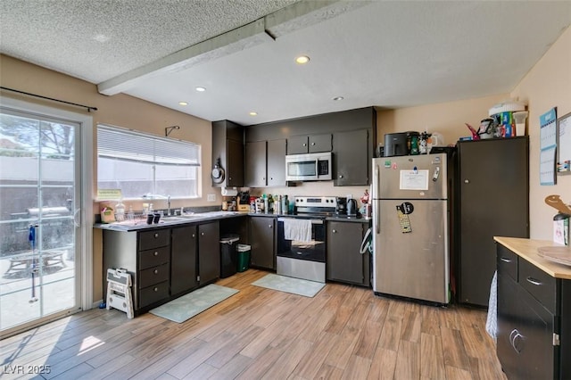 kitchen with appliances with stainless steel finishes, light wood-style floors, recessed lighting, a sink, and dark cabinets