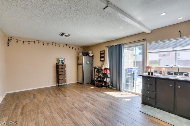 misc room with a sink, a textured ceiling, healthy amount of natural light, light wood-type flooring, and baseboards