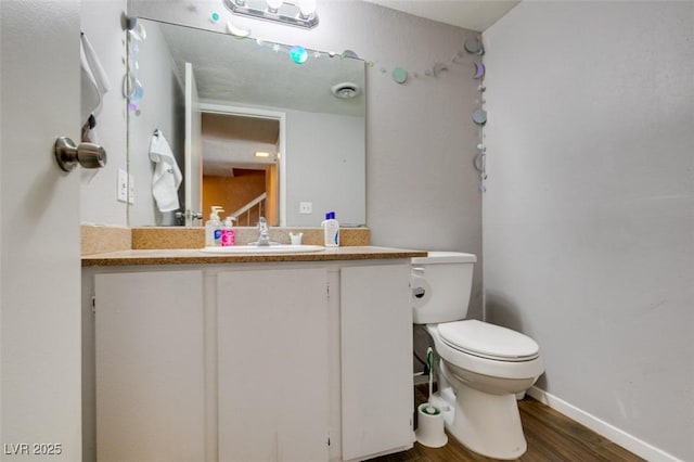 bathroom featuring wood finished floors, toilet, vanity, and baseboards