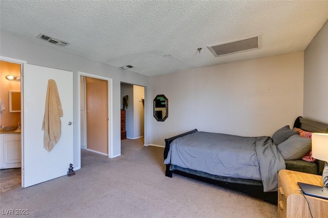 bedroom featuring attic access, light carpet, a textured ceiling, baseboards, and ensuite bath
