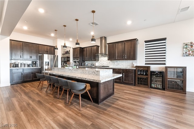 212 Harris Peak St, Las Vegas, NV 89138 - kitchen with stainless steel appliances, wine cooler, wall chimney exhaust hood, dark brown cabinetry, and decorative backsplash