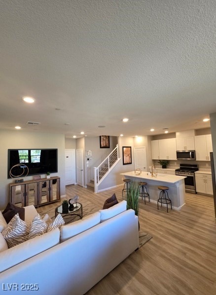 living room featuring stairway, a textured ceiling, recessed lighting, and light wood-style flooring