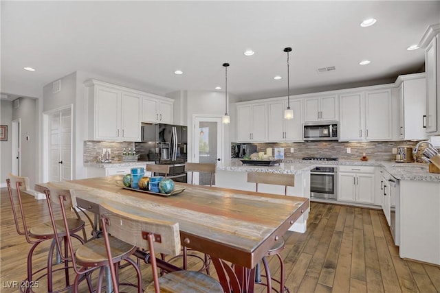 kitchen featuring stainless steel appliances, backsplash, white cabinets, light wood-style flooring, and a kitchen island