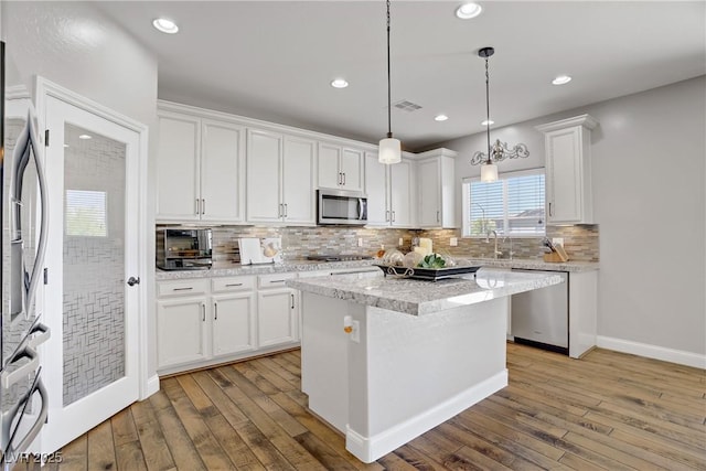 kitchen with stainless steel appliances, light wood-style floors, white cabinets, backsplash, and a sink