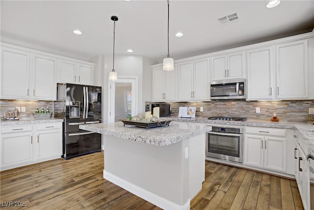 kitchen featuring appliances with stainless steel finishes, white cabinetry, wood-type flooring, backsplash, and a center island