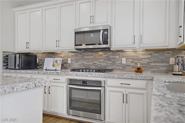 kitchen with stainless steel appliances, white cabinets, decorative backsplash, and light stone counters