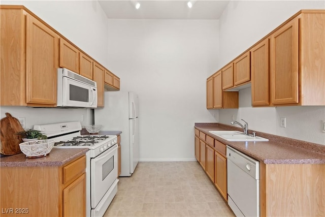 kitchen with white appliances, a sink, baseboards, and a towering ceiling