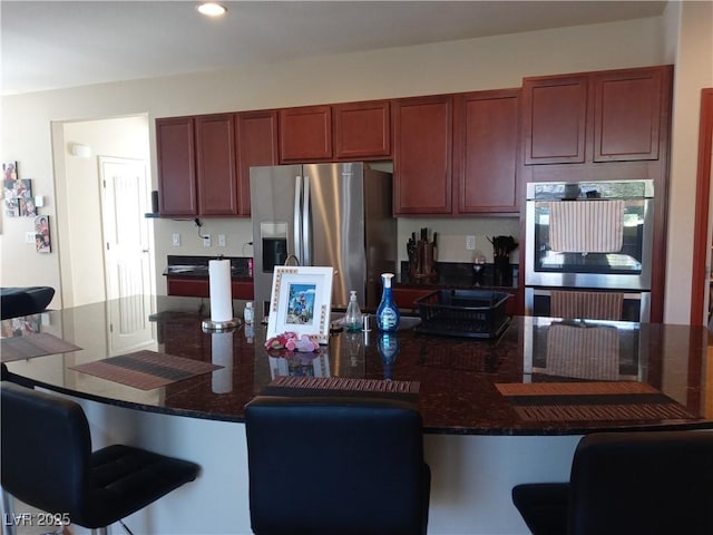 kitchen with stainless steel appliances, a kitchen breakfast bar, recessed lighting, and dark stone counters