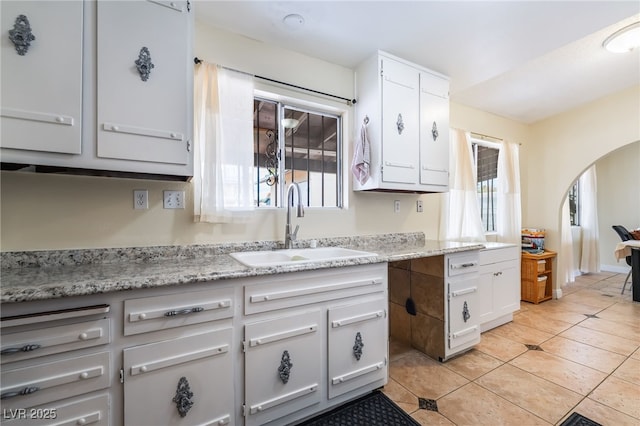 kitchen featuring a sink, arched walkways, white cabinetry, and light tile patterned flooring