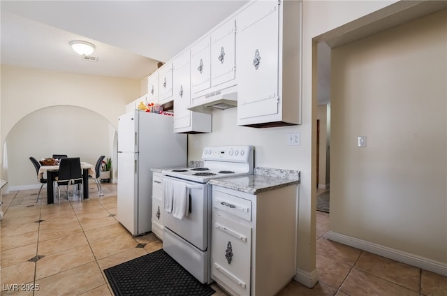kitchen with white appliances, arched walkways, under cabinet range hood, light tile patterned floors, and white cabinets