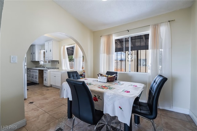 dining space with arched walkways, lofted ceiling, light tile patterned floors, and baseboards