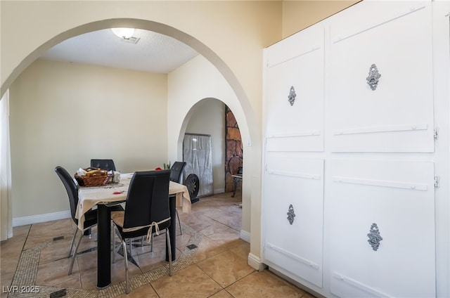 dining area with arched walkways, light tile patterned floors, and baseboards