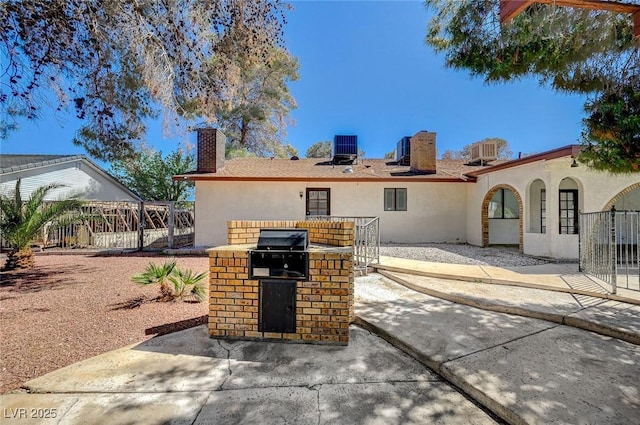 rear view of property with a chimney, stucco siding, an outdoor kitchen, and a patio