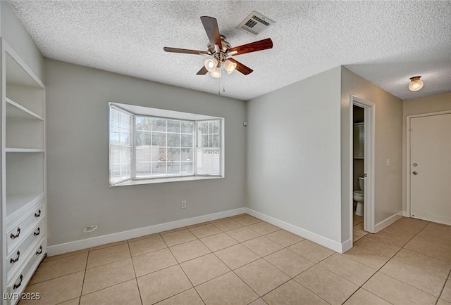 spare room with a ceiling fan, a textured ceiling, light tile patterned floors, and baseboards