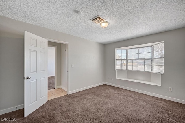 carpeted empty room featuring tile patterned floors, a textured ceiling, and baseboards