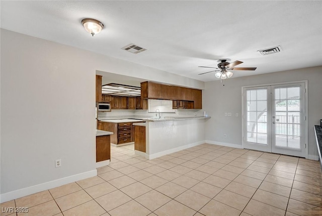 kitchen featuring stainless steel microwave, a peninsula, light countertops, ceiling fan, and baseboards