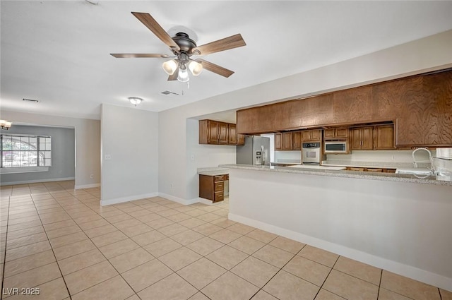 kitchen with appliances with stainless steel finishes, a sink, a peninsula, and brown cabinetry