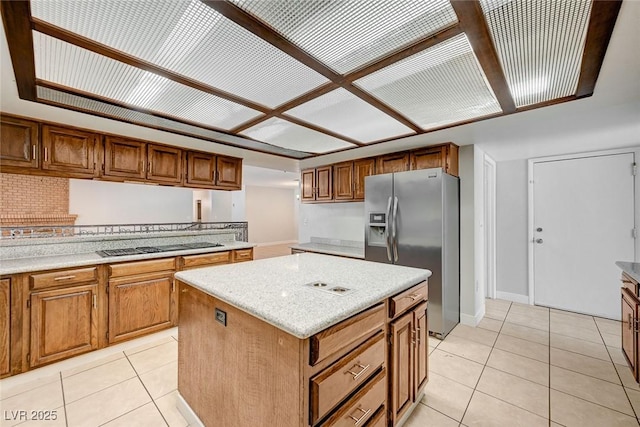 kitchen with stainless steel refrigerator with ice dispenser, light tile patterned floors, a kitchen island, and black stovetop