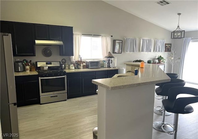 kitchen with stainless steel appliances, under cabinet range hood, a breakfast bar, healthy amount of natural light, and high vaulted ceiling