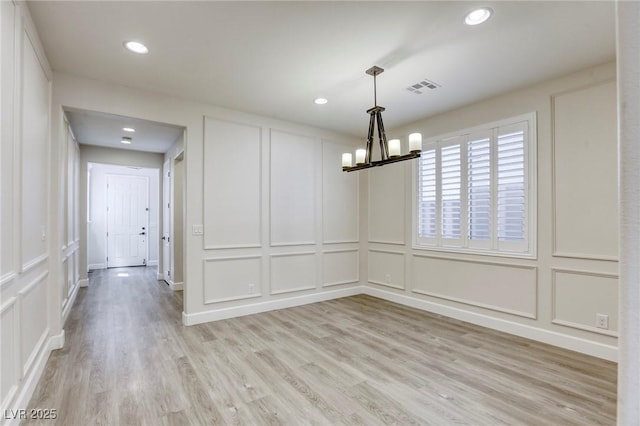unfurnished dining area featuring a decorative wall, a chandelier, light wood-style flooring, and recessed lighting