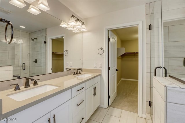 bathroom with a stall shower, double vanity, a walk in closet, tile patterned flooring, and baseboards