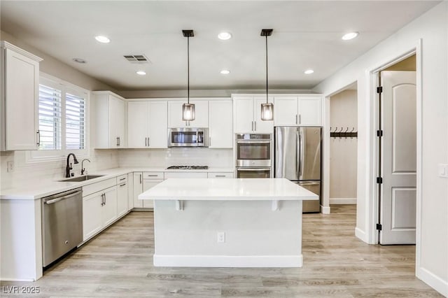 kitchen with stainless steel appliances, a sink, a kitchen island, white cabinetry, and tasteful backsplash