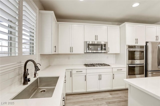 kitchen with appliances with stainless steel finishes, a sink, backsplash, white cabinetry, and recessed lighting