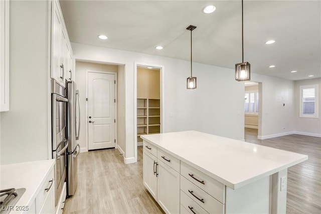 kitchen featuring white cabinets, baseboards, light wood finished floors, light countertops, and hanging light fixtures
