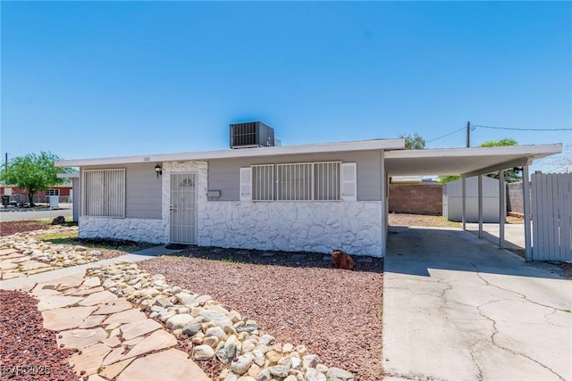 view of front of property with driveway, central AC unit, a carport, fence, and stone siding