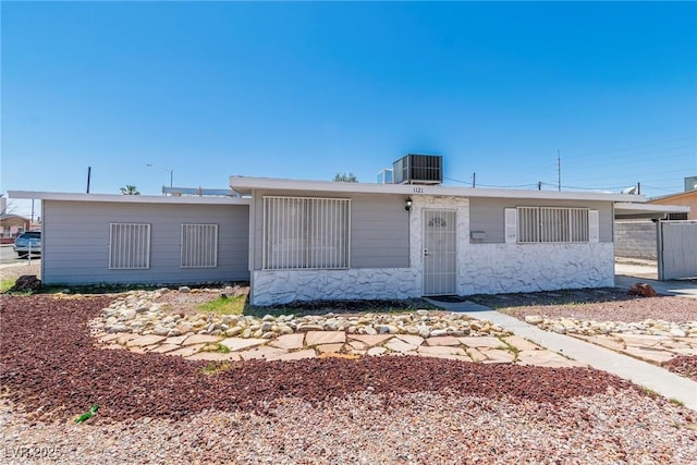 view of front of property featuring central air condition unit, stone siding, and fence