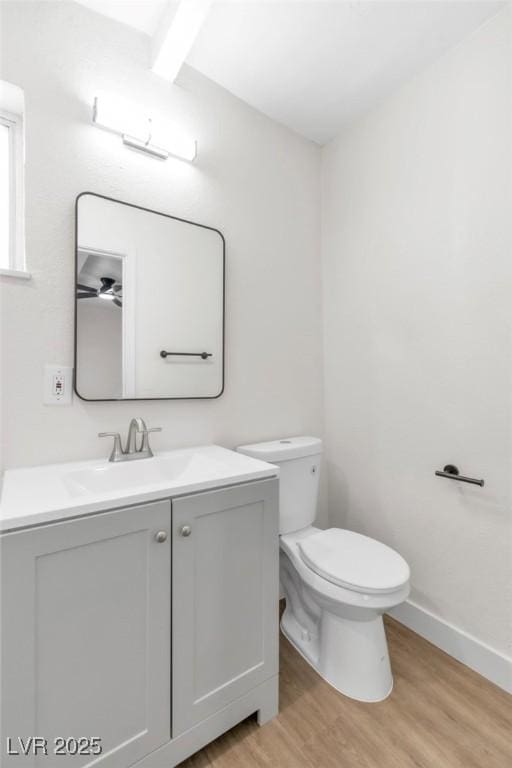 half bathroom with wood finished floors, toilet, vanity, and baseboards