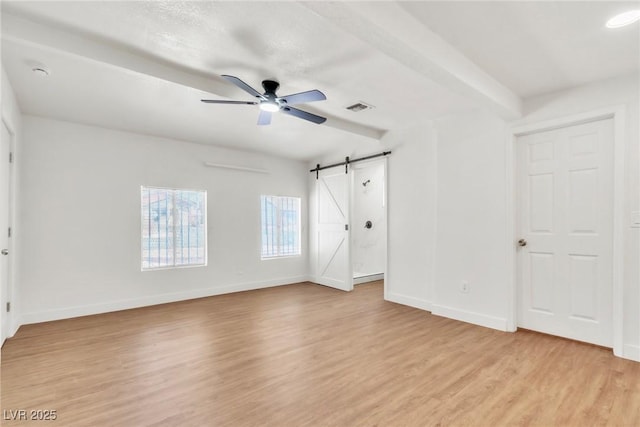 unfurnished bedroom featuring a barn door, light wood-style floors, baseboards, beamed ceiling, and a ceiling fan