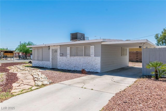 view of front of house with central AC, fence, concrete driveway, stone siding, and a carport