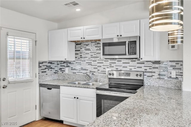 kitchen featuring appliances with stainless steel finishes, a sink, white cabinetry, tasteful backsplash, and light stone countertops