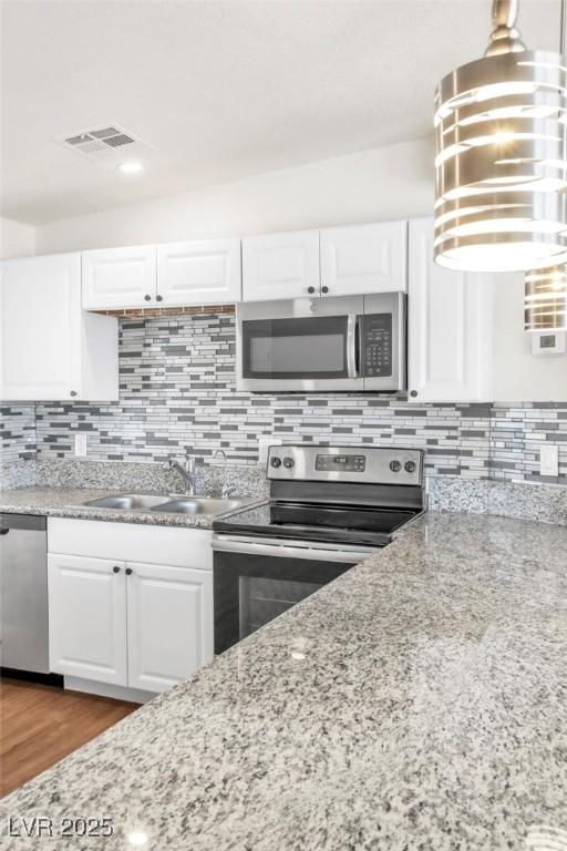 kitchen with stainless steel appliances, a sink, white cabinets, and backsplash