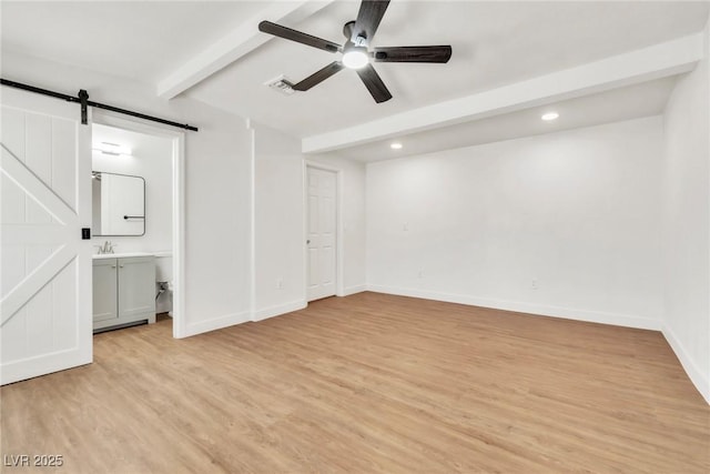 unfurnished bedroom featuring beam ceiling, a barn door, light wood-style flooring, recessed lighting, and baseboards