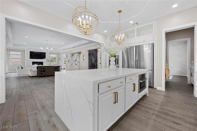 4220 San Alivia Ct, Las Vegas, NV 89141 - kitchen featuring a raised ceiling, a chandelier, stainless steel appliances, wood finished floors, and light stone countertops