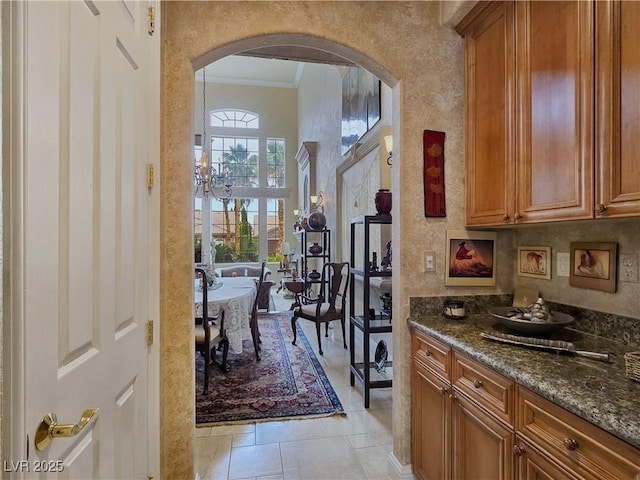 5445 Pendini Point Ct, Las Vegas, NV 89141 - bar area featuring arched walkways, crown molding, a textured wall, light tile patterned floors, and baseboards