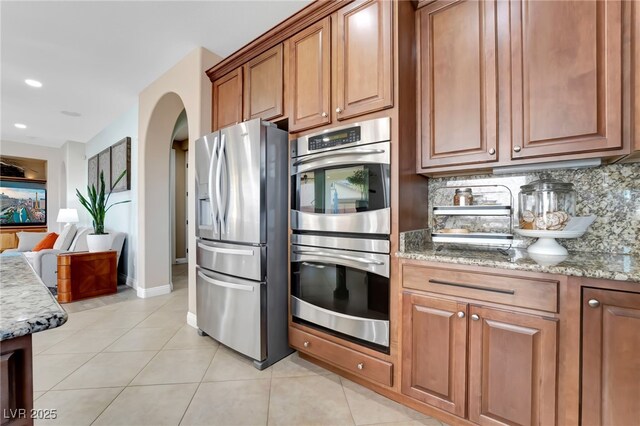 7778 Villa Montara St, Las Vegas, NV 89123 - kitchen with stainless steel appliances, light stone counters, light tile patterned floors, brown cabinets, and open floor plan