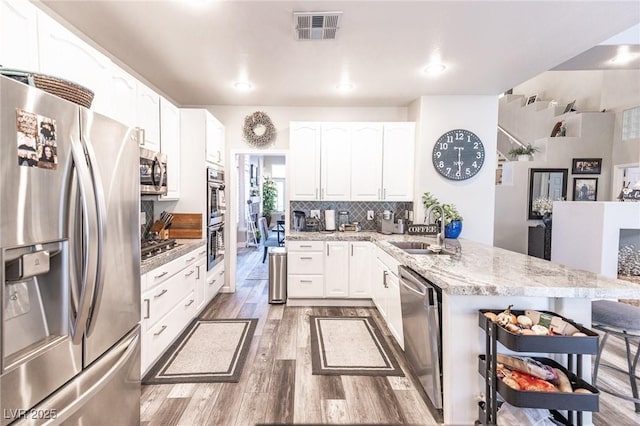 53 Grossinger Ct, Henderson, NV 89074 - kitchen featuring appliances with stainless steel finishes, a sink, a peninsula, wood finished floors, and light stone counters