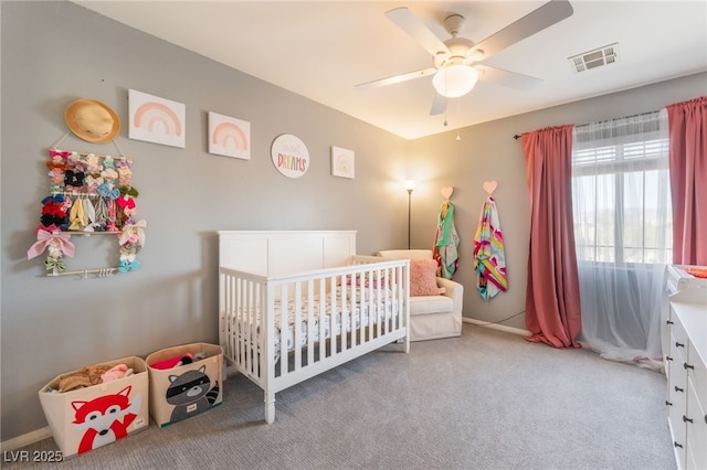 carpeted bedroom featuring a nursery area, ceiling fan, and baseboards