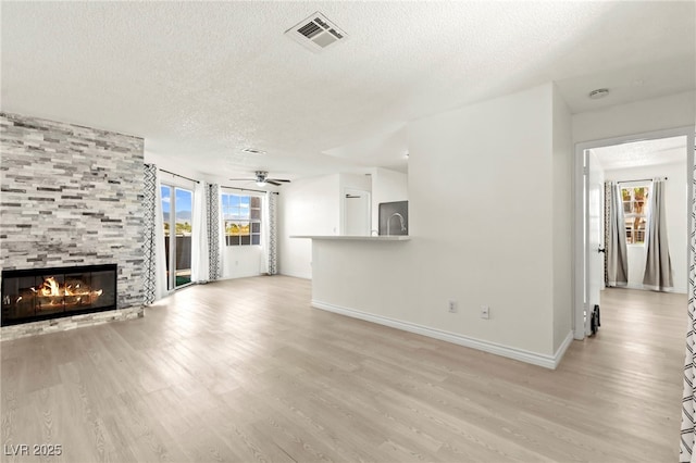 unfurnished living room with a textured ceiling, light wood-style floors, baseboards, a tile fireplace, and a ceiling fan
