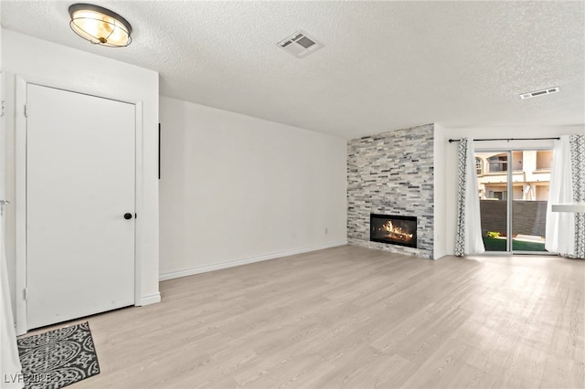 unfurnished living room with a textured ceiling, light wood-style flooring, a tile fireplace, and baseboards