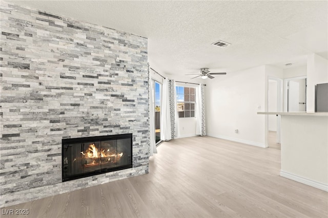 unfurnished living room with baseboards, a ceiling fan, a textured ceiling, a fireplace, and wood finished floors