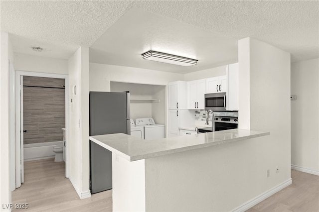 kitchen with independent washer and dryer, appliances with stainless steel finishes, a textured ceiling, light wood-style floors, and light countertops