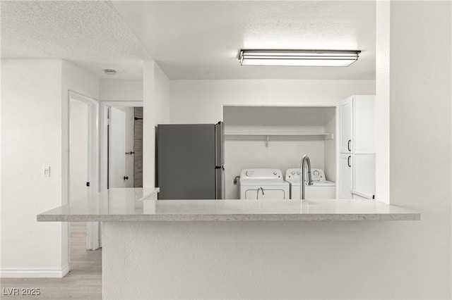 kitchen with freestanding refrigerator, washer and clothes dryer, white cabinets, light wood-type flooring, and light countertops