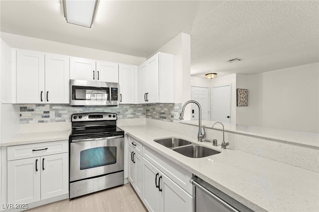 kitchen featuring appliances with stainless steel finishes, a sink, white cabinetry, backsplash, and a textured ceiling