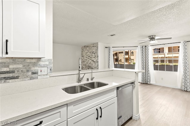 kitchen with a sink, a textured ceiling, dishwasher, backsplash, and white cabinetry