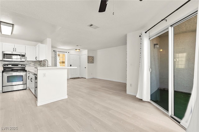 kitchen with stainless steel appliances, light wood finished floors, light countertops, a textured ceiling, and a peninsula